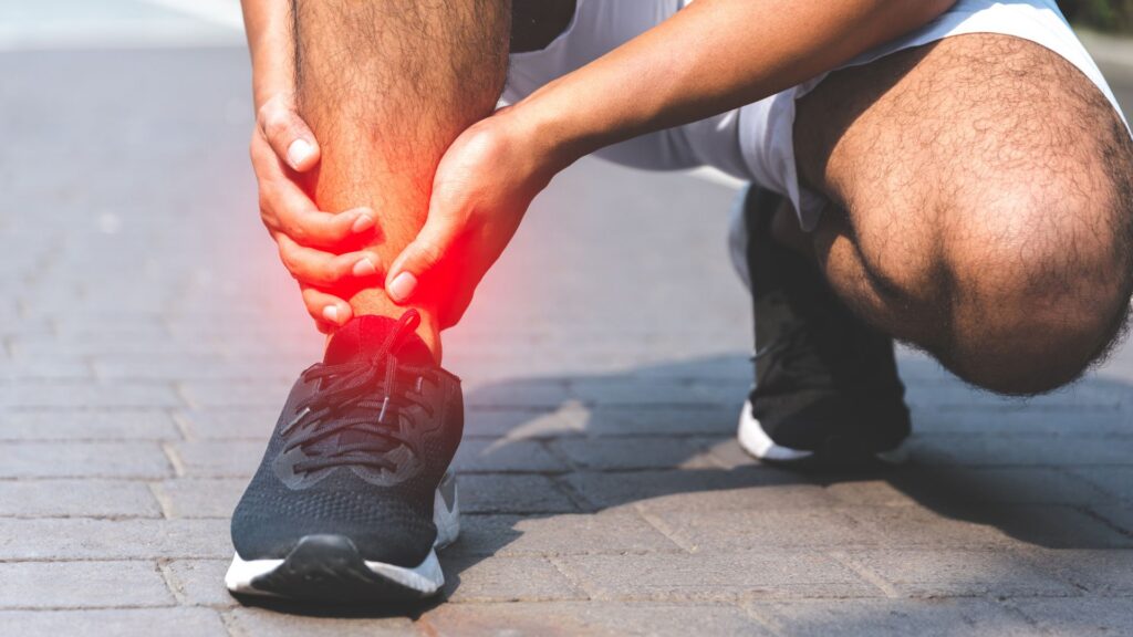 A person in athletic gear kneels on a paved path, clutching their painful ankle highlighted with red, conveying injury. The tone is urgent and concerned.