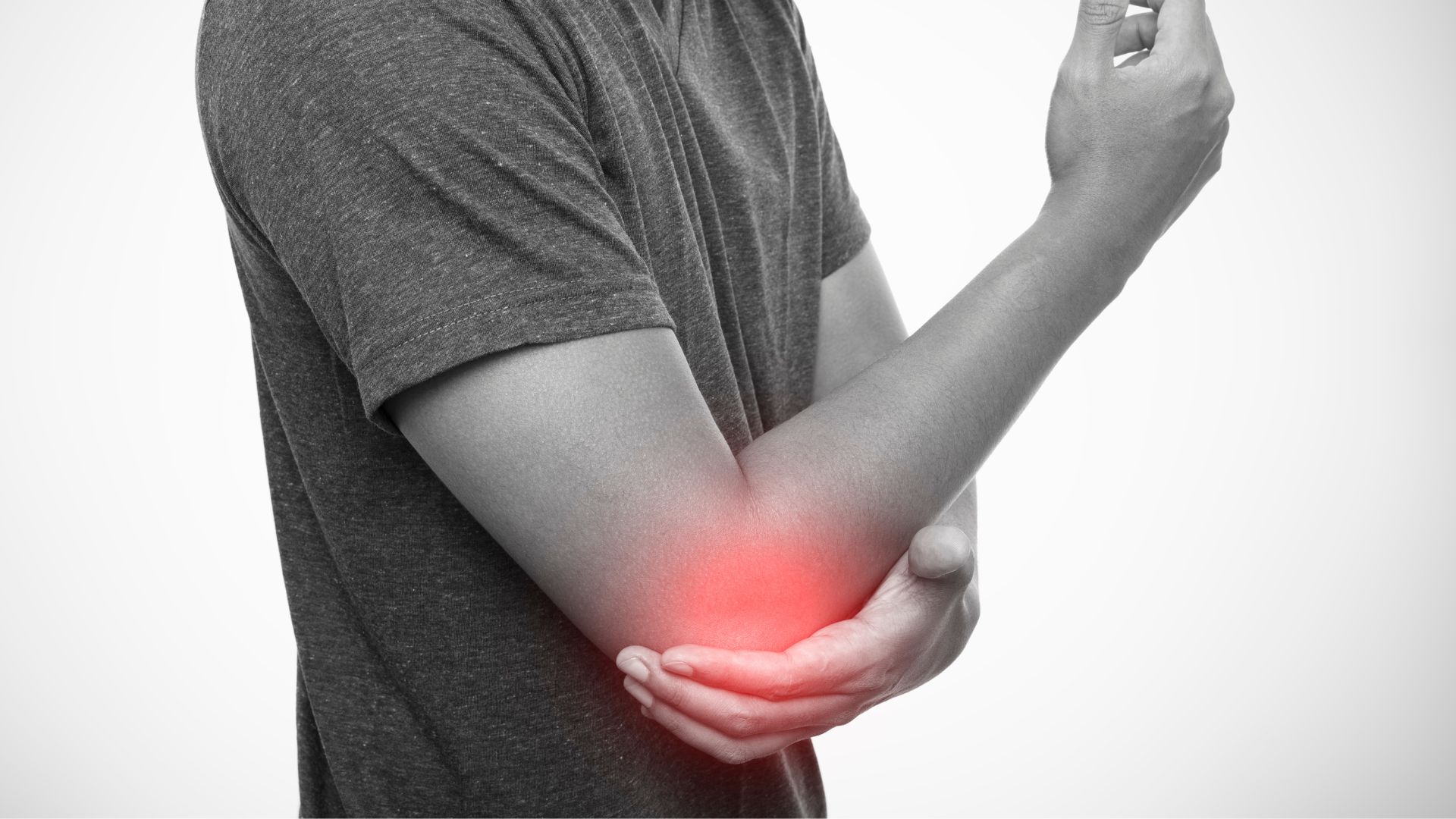 A person in a gray t-shirt holds their elbow, highlighted with a red glow, indicating pain or injury, conveying discomfort or concern.