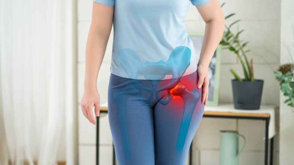 A woman in a light blue shirt and pants holds her hip, indicating pain. An overlay shows a highlighted hip joint in red, emphasizing discomfort.