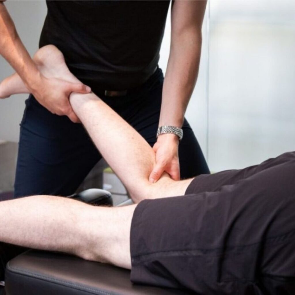 Person receiving leg massage therapy on a treatment table. Therapist uses both hands, conveying a professional, calming, and therapeutic atmosphere.